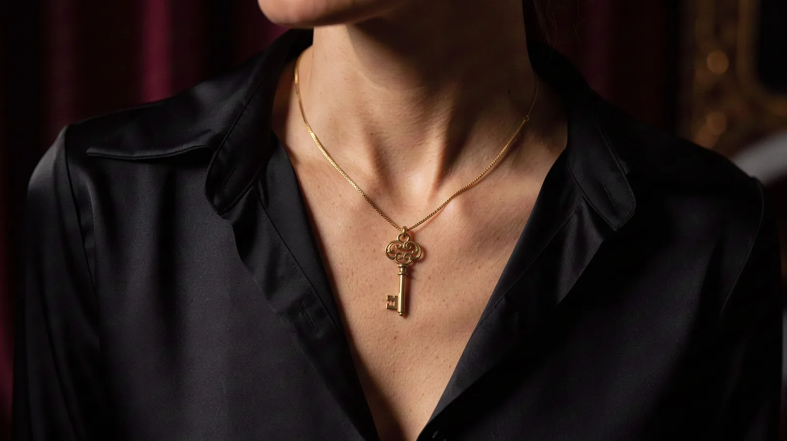 Petite clé dorée en pendentif au cou d'une femme vêtue de noir, visage hors cadre.
